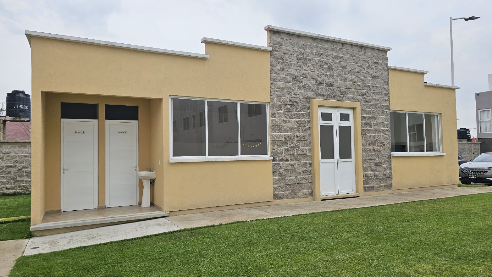Casa club del desarrollo con salón de eventos, muro de piedra y sanitarios independientes frente al jardín