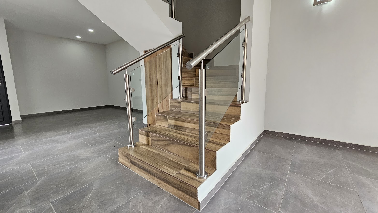 Recibidor y estancia con piso de porcelanato gris tipo mármol y escalera de madera con barandal de acero inoxidable y cristal